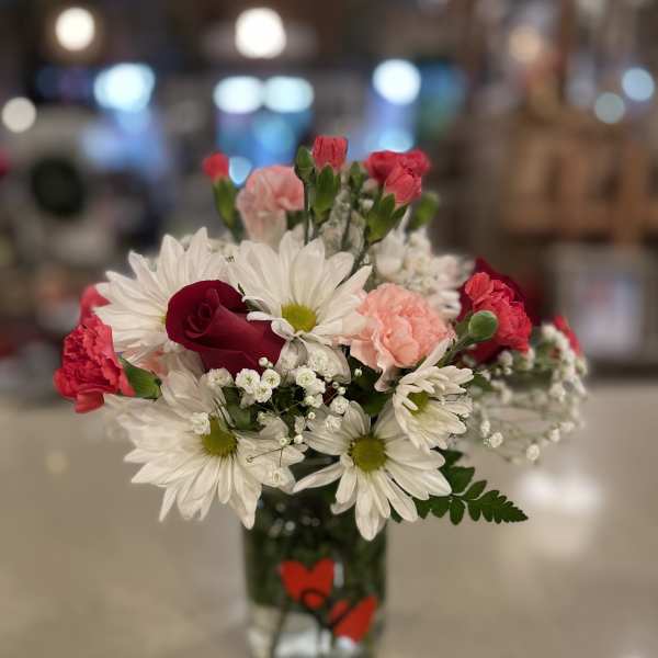 Bouquet of white daisies, red roses, and pink carnations in a glass vase
