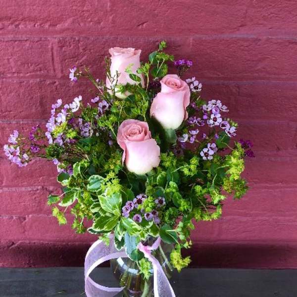 Pink roses in a glass vase with purple filler flowers and a ribbon