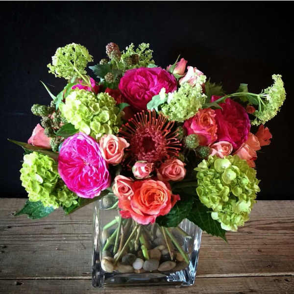 Bright mixed bouquet in a clear square vase with pink and green blooms