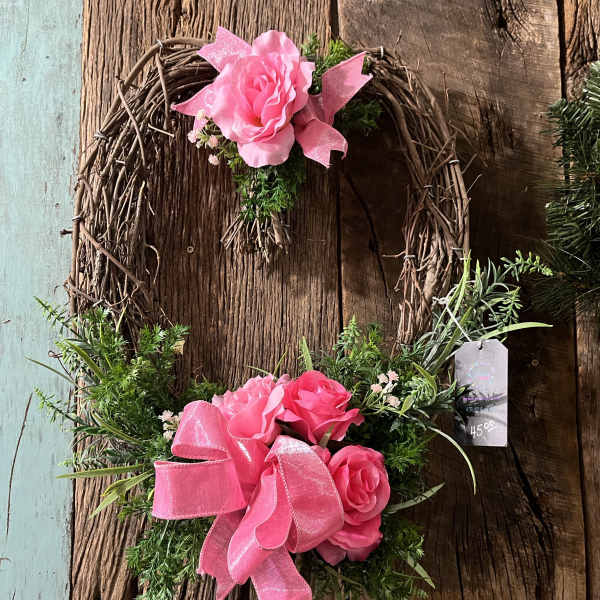 Two pink rose wreaths with ribbon accents on a rustic wood background