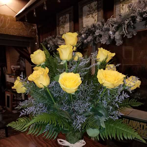 Yellow roses arranged in a clear glass vase with a white ribbon