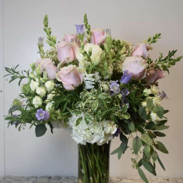 Large bouquet of pale pink roses, white hydrangea, and purple flowers in a glass vase