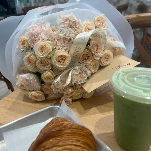 Bouquet of pale peach roses and ruffled carnations wrapped in white paper