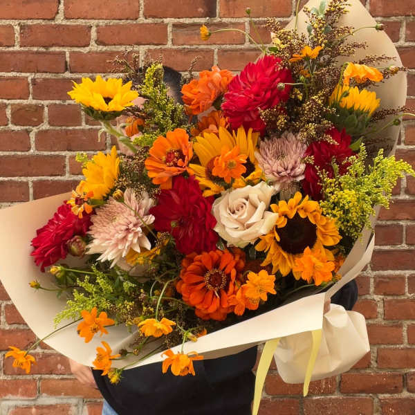 Large bouquet of sunflowers, dahlias, and roses wrapped in cream paper