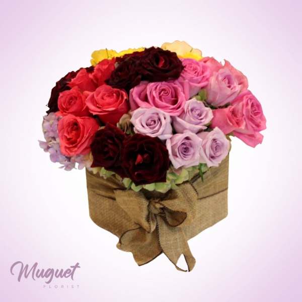 Round bouquet of pink, red, and lavender roses in a burlap-wrapped box