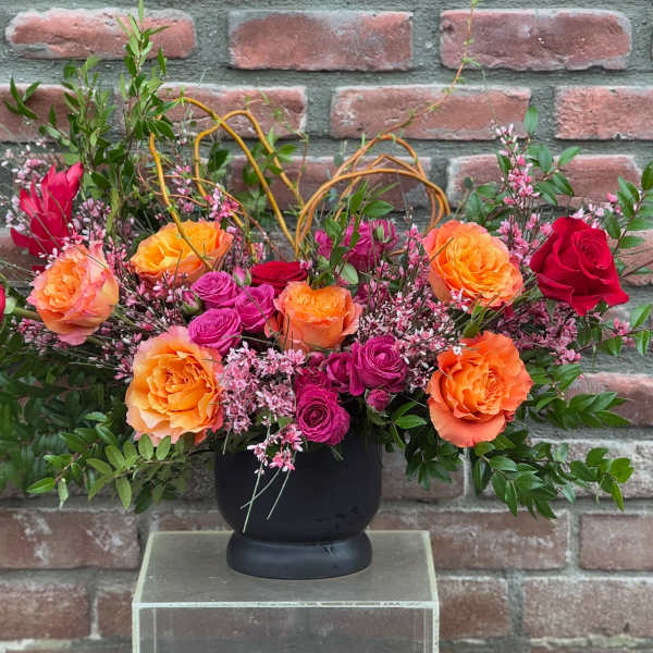 Arrangement of orange, pink, and red roses in a black vase