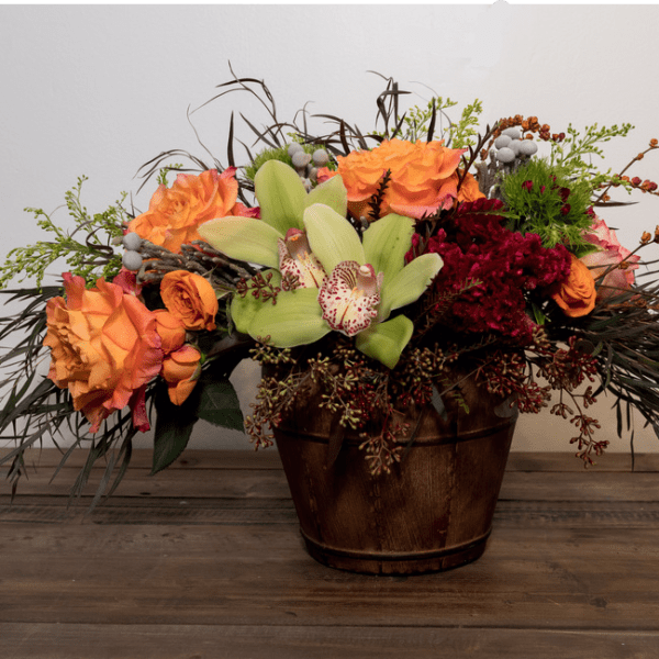 Orange and burgundy floral arrangement in a wooden container