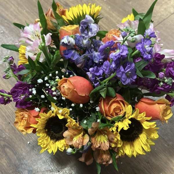 Compact bouquet of yellow sunflowers, orange roses, and purple flowers in a bright mixed arrangement