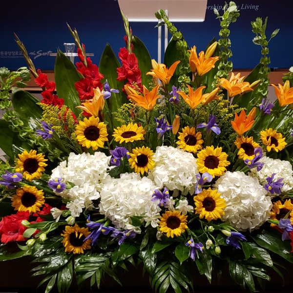 Large altar-style arrangement with sunflowers, white hydrangeas, orange lilies and mixed bright flowers