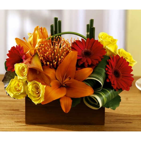 Orange and red floral arrangement with yellow roses in a wooden box
