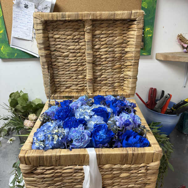 Blue roses and hydrangeas arranged in a woven basket with a white ribbon
