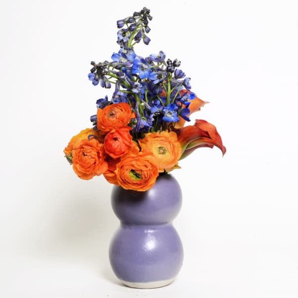 Orange and blue flowers arranged in a purple vase