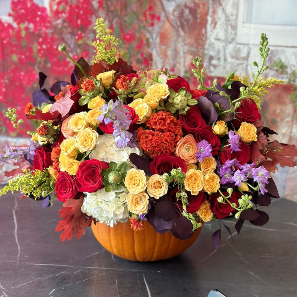 Mixed bouquet in a pumpkin container with red, yellow, and purple flowers