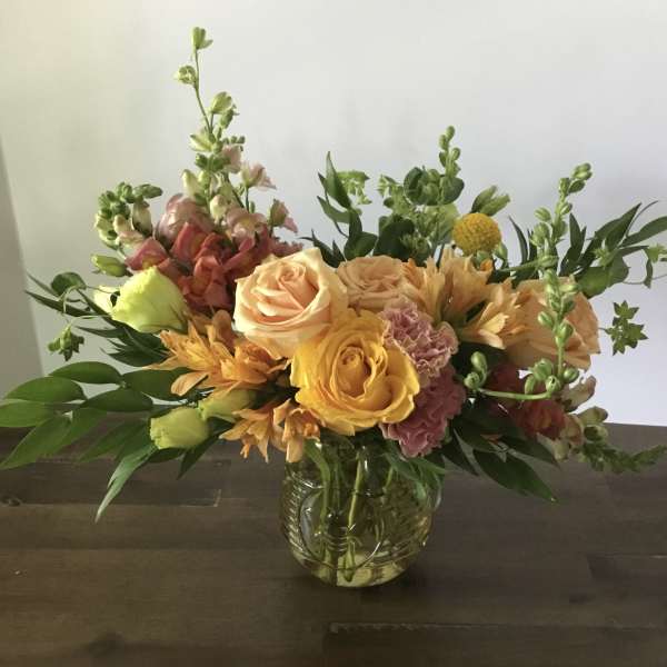 Mixed bouquet of peach, yellow, and pink flowers in a glass vase