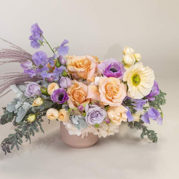Pastel bouquet of roses, poppies, and purple blooms in a pink vase