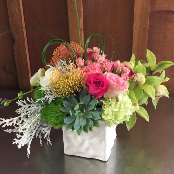 Mixed floral arrangement in a white square vase with pink roses and green succulents