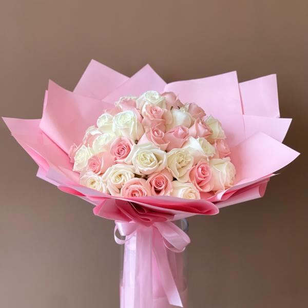 Bouquet of pink and white roses wrapped in pink paper in a glass vase