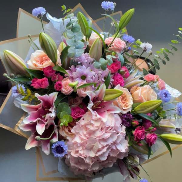 Mixed bouquet with pink lilies, roses, hydrangea, and blue accent flowers