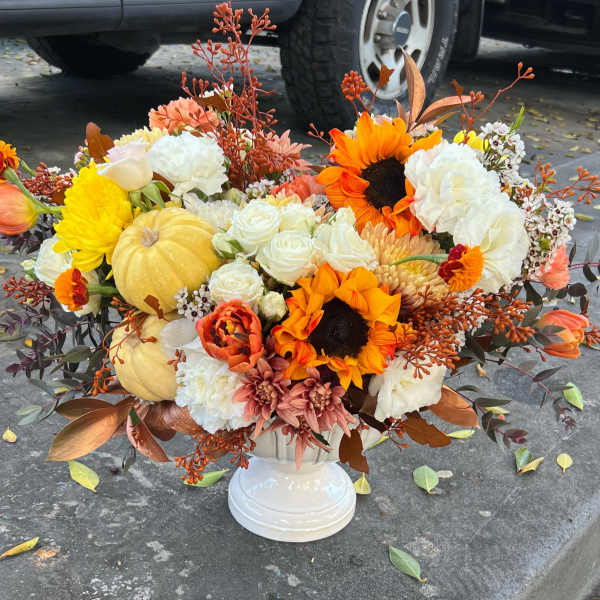 Autumn floral arrangement with sunflowers, white roses, and pumpkins in a white vase