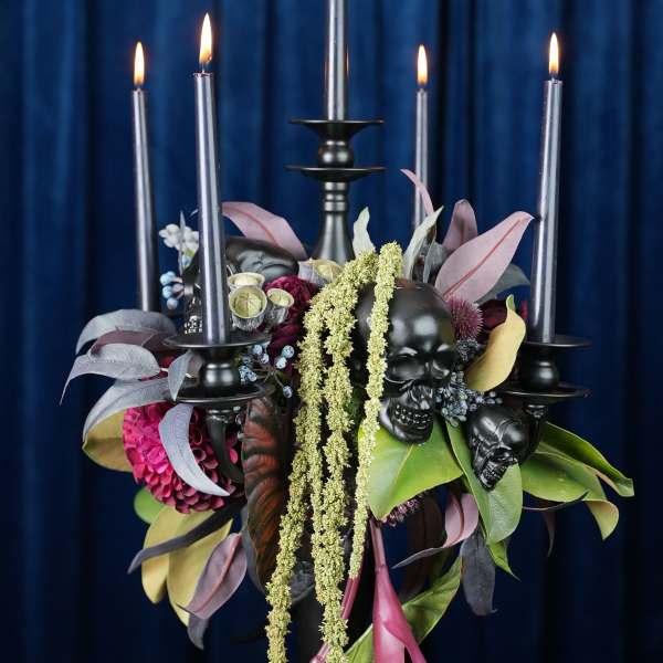Black candelabra with lit candles and a dark floral arrangement featuring skulls