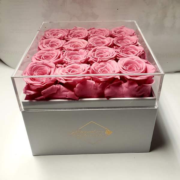 Pink roses arranged in a clear square box on a gray base