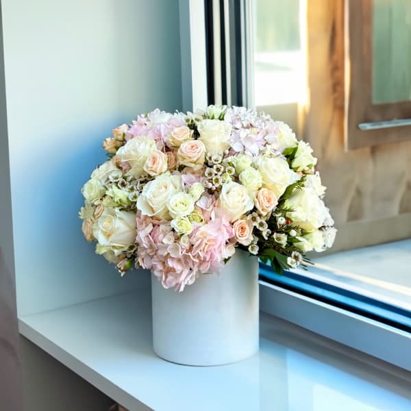 Round bouquet of pale pink and white roses in a white vase