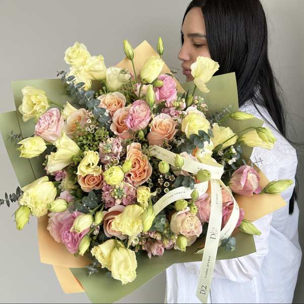 Large bouquet of pale yellow and peach flowers wrapped in green and peach paper