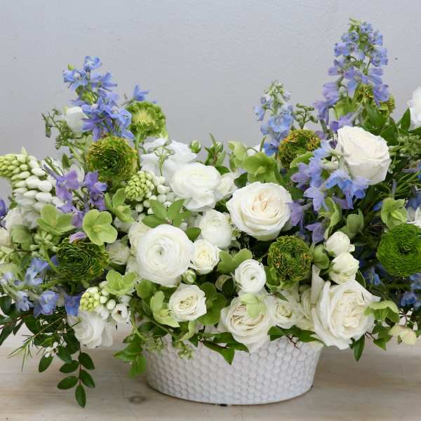 Low arrangement of white roses and ranunculus with blue flowers in a white ceramic bowl