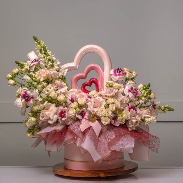 Pink and white floral arrangement in a round box with heart decorations