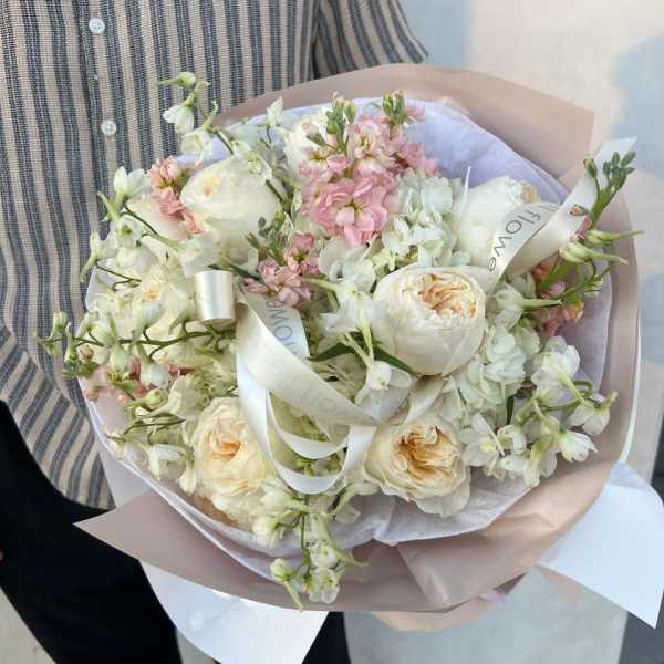 Hand-tied bouquet of white and blush flowers wrapped in pale paper