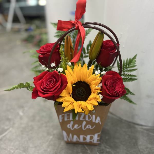 Basket arrangement with red roses and a sunflower, tied with a red ribbon