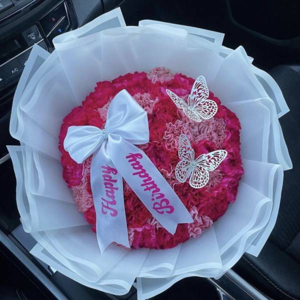 Round bouquet of pink carnations with a white ribbon and butterfly decorations
