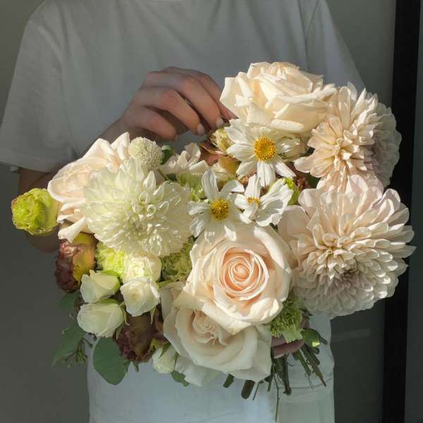 Handheld bouquet of cream roses, white daisies, and pale dahlias