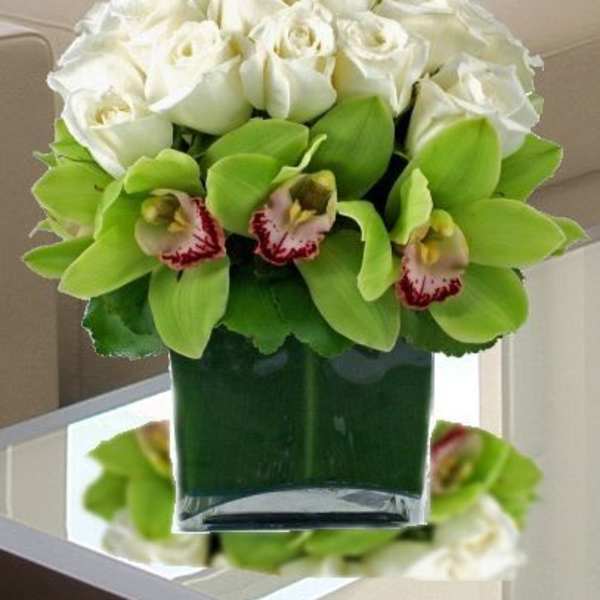 White roses and green orchids arranged in a glass vase