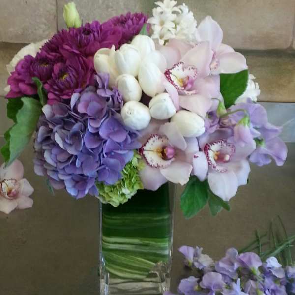 Purple and white flowers arranged in a tall glass vase