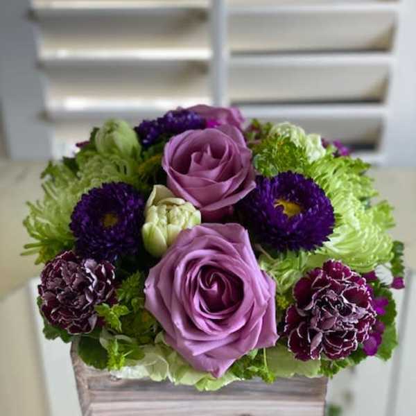 Purple roses and dark blooms arranged in a wooden box