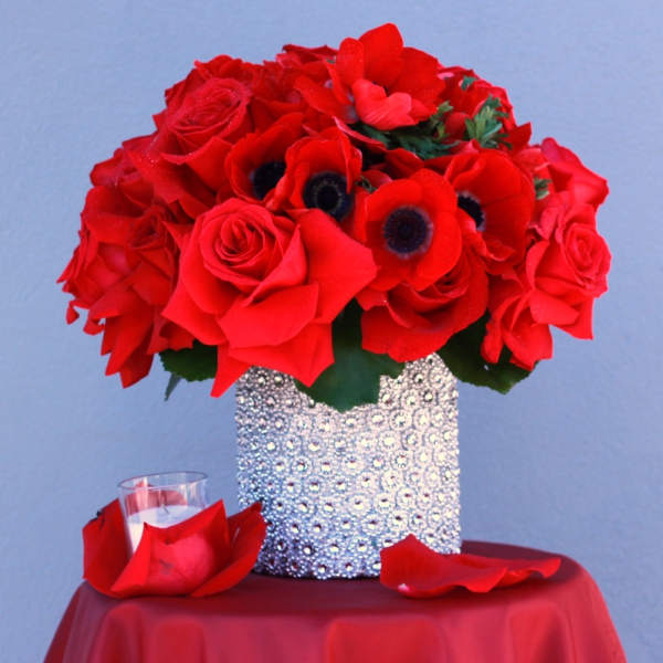 Red rose bouquet in a silver textured vase with red petals on a table