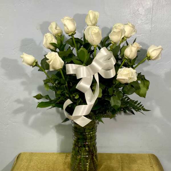 White roses arranged in a glass vase with a white ribbon