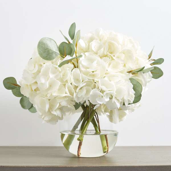 White hydrangea bouquet in a clear glass bowl vase with eucalyptus