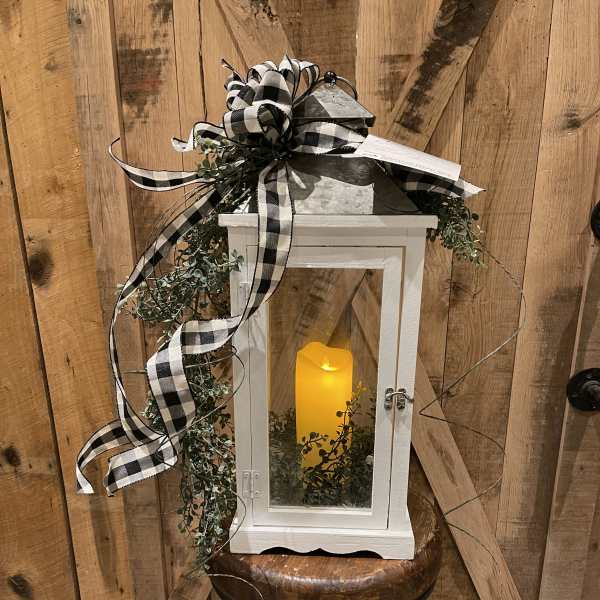 White lantern with a glowing candle, greenery, and black-and-white ribbon