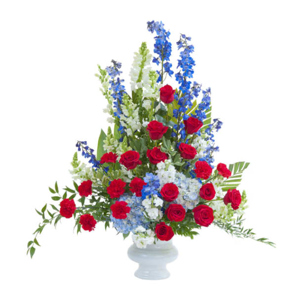 Tall arrangement of red roses, blue delphinium, and white flowers in a white vase