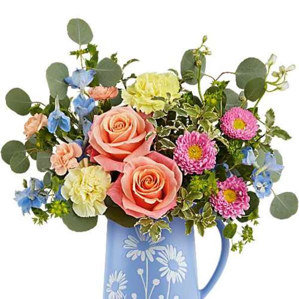 Bouquet of pink roses, blue flowers, and daisies in a blue pitcher vase