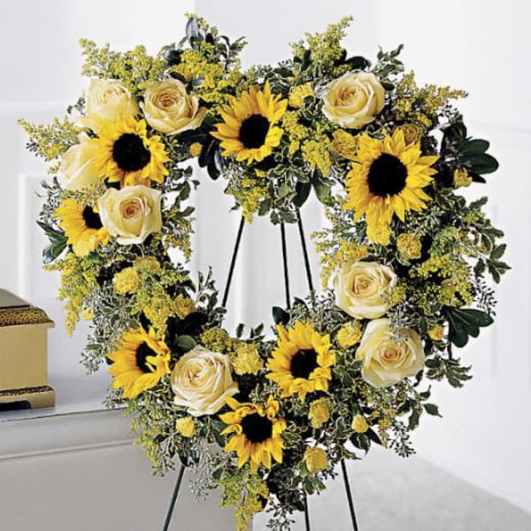 Heart-shaped floral wreath with sunflowers and cream roses on a stand