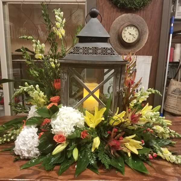 Low floral centerpiece with white hydrangeas, yellow lilies, and coral roses around a lantern.