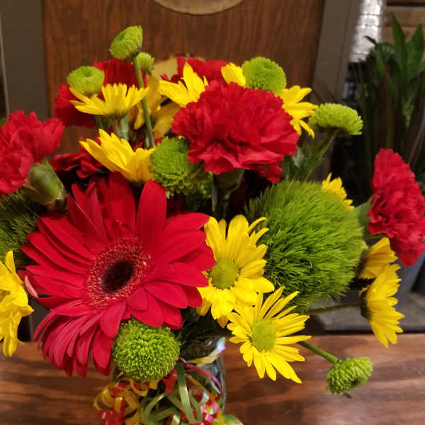 Bouquet of red gerbera daisies, yellow daisies, and green pompons in a glass vase
