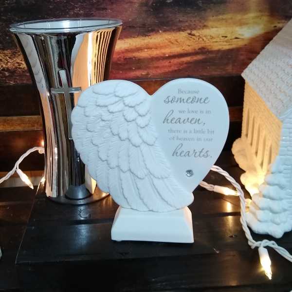 Heart-shaped angel memorial plaque beside a silver vase with a cross