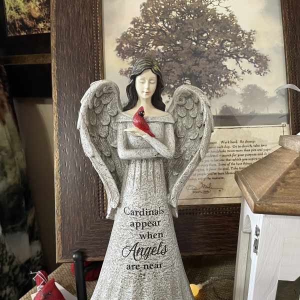 Angel figurine holding a red cardinal with small flowers at the base