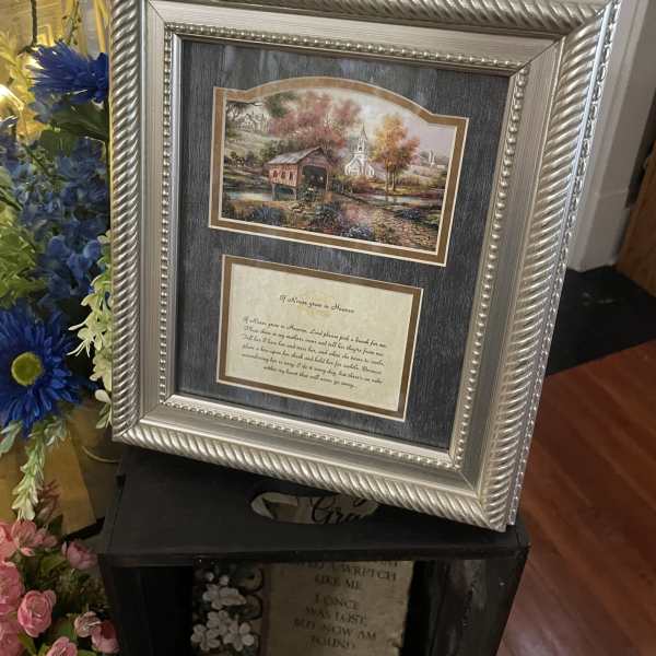 Framed memorial print with blue and pink flowers beside it