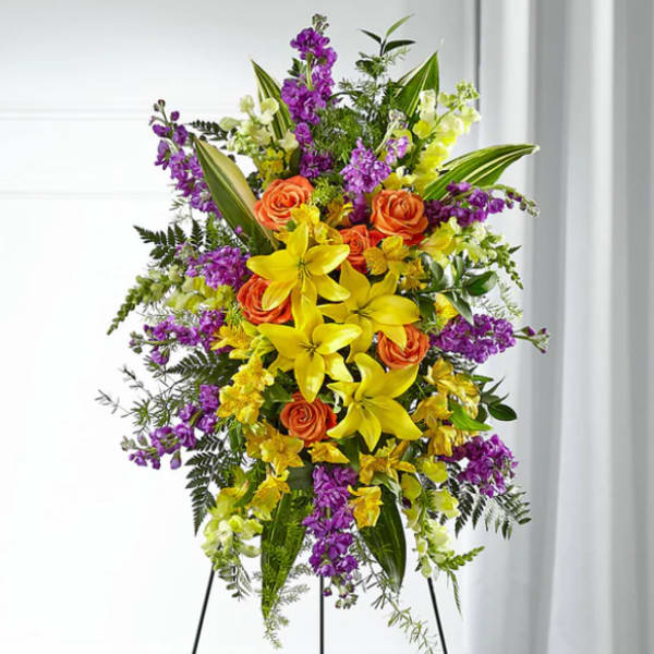 Tall standing floral spray with yellow lilies, orange roses, and purple flowers