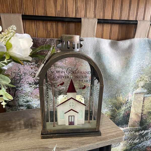 Memorial lantern with a church scene and white flowers beside it